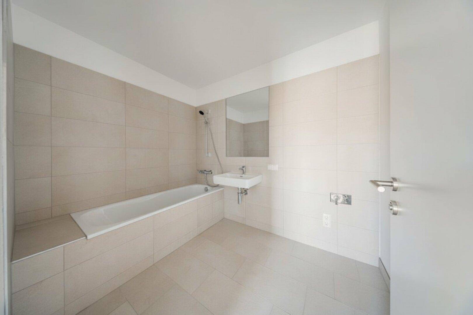Modernes Badezimmer mit Badewanne, Waschbecken und hellen Fliesen an Wänden und Boden.