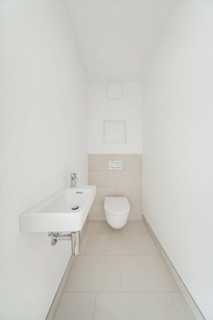 Separates Gäste-WC mit wandhängendem WC, kleinem Waschbecken und hellen Fliesen.