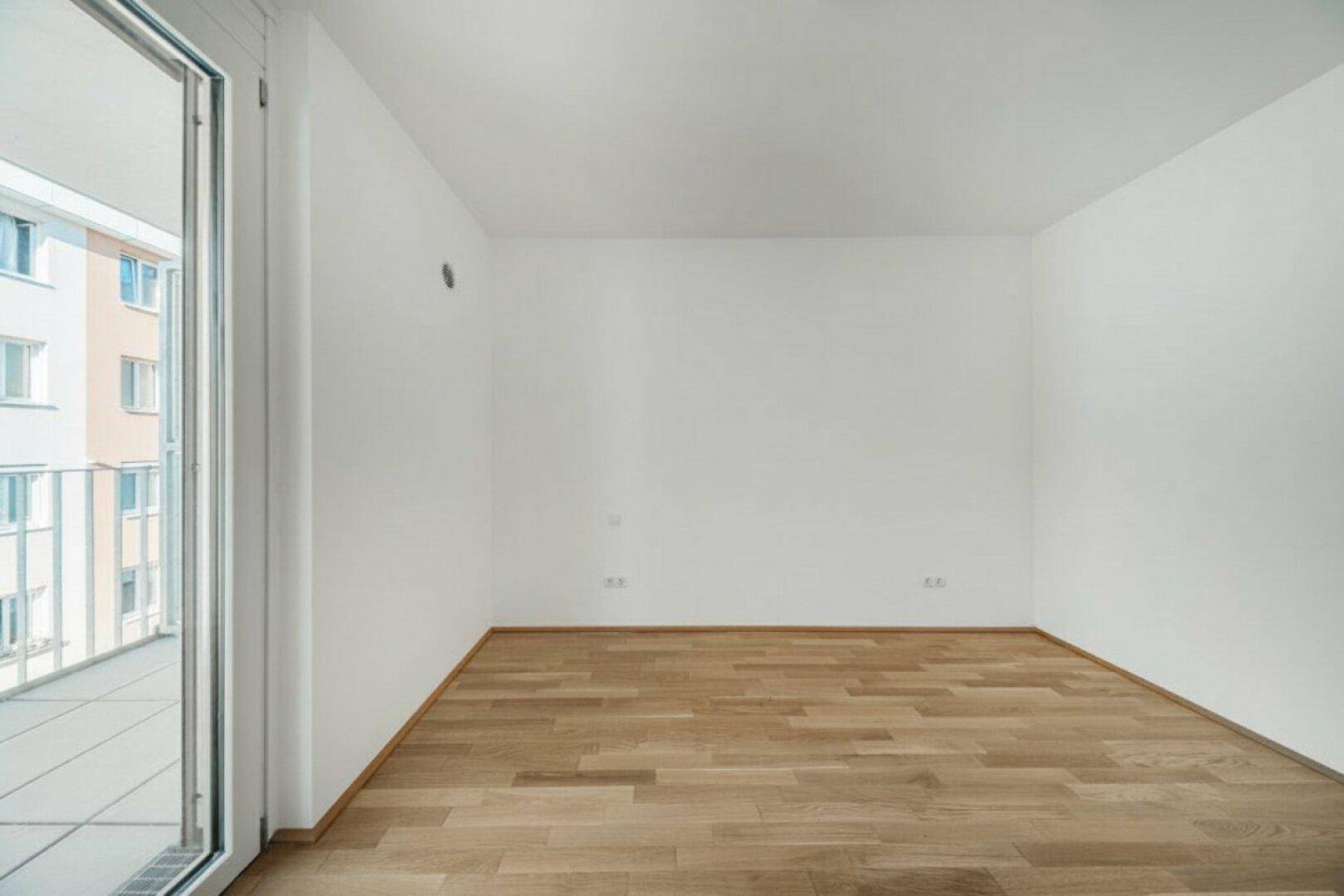 Leeres Schlafzimmer mit hellem Parkettboden und direktem Zugang zu einem Außenbereich.
