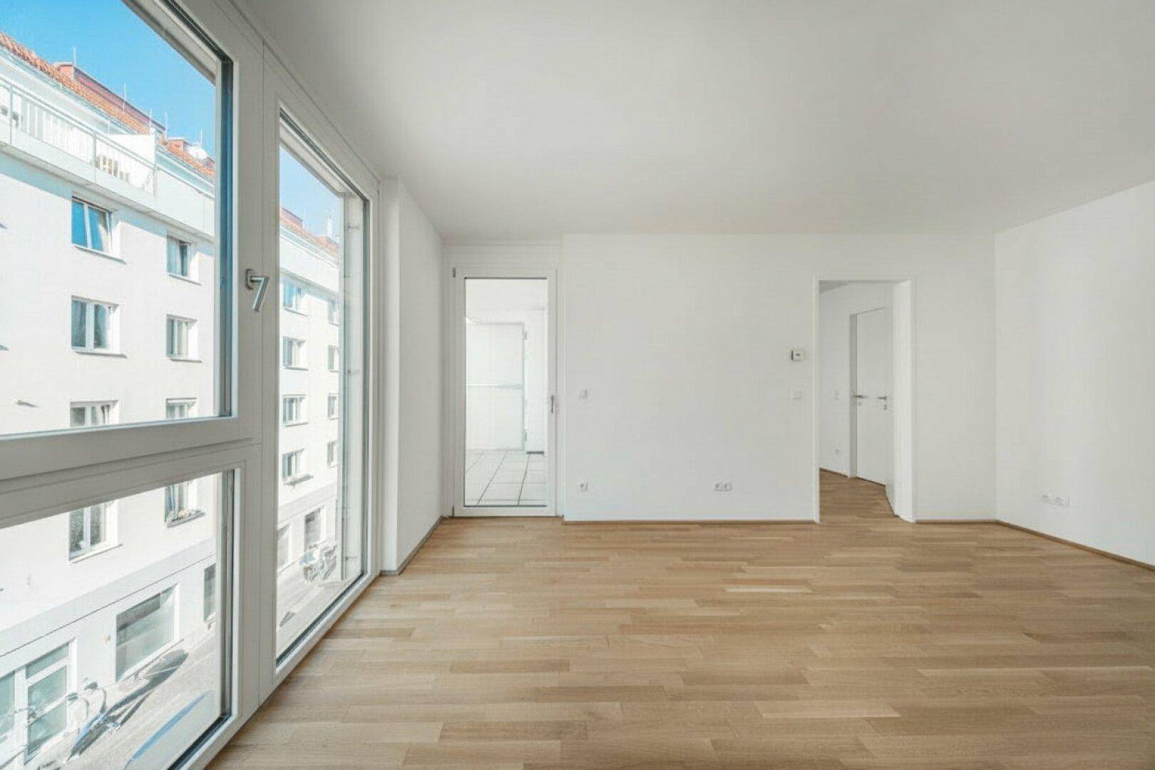 Geräumiges, leeres Zimmer mit Parkettboden, großen Fenstern und Stadtblick.