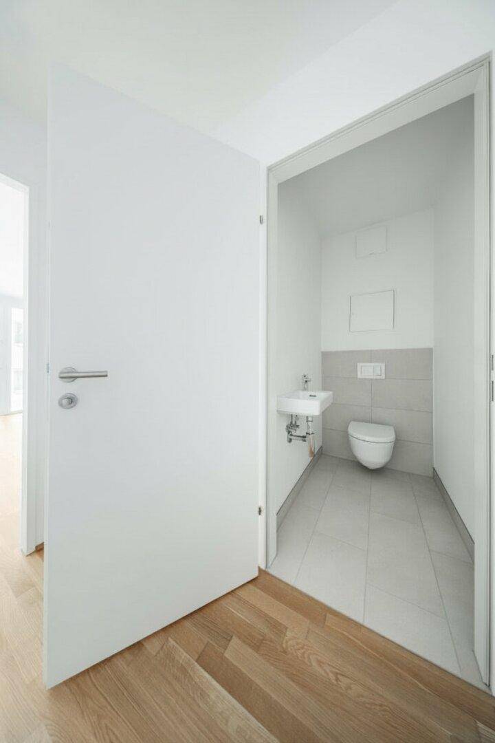 Modernes Gäste-WC mit Wand-WC, kleinem Waschbecken und hellen Fliesen.