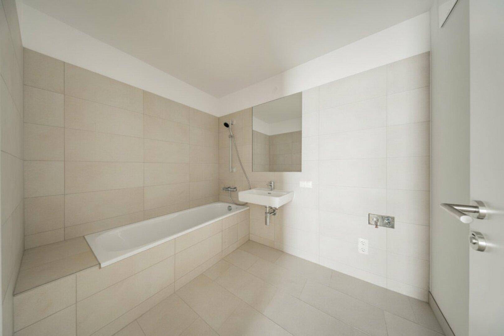 Helles Badezimmer mit Badewanne, Waschbecken und Spiegel, komplett gefliest.