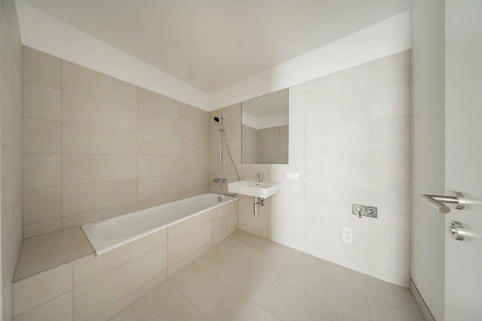 Helles Badezimmer mit Badewanne, Waschbecken und Spiegel, komplett gefliest.