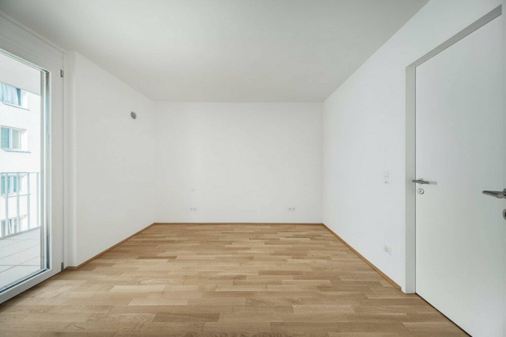 Leerer Raum mit Parkettboden, weißer Tür und Zugang zum Außenbereich.