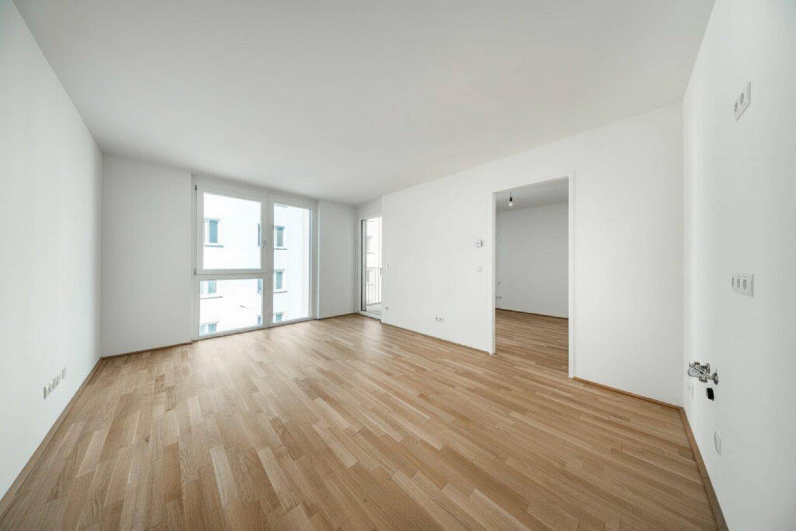 Geräumiger, leerer Raum mit Parkettboden und großen Fenstern für viel Licht.