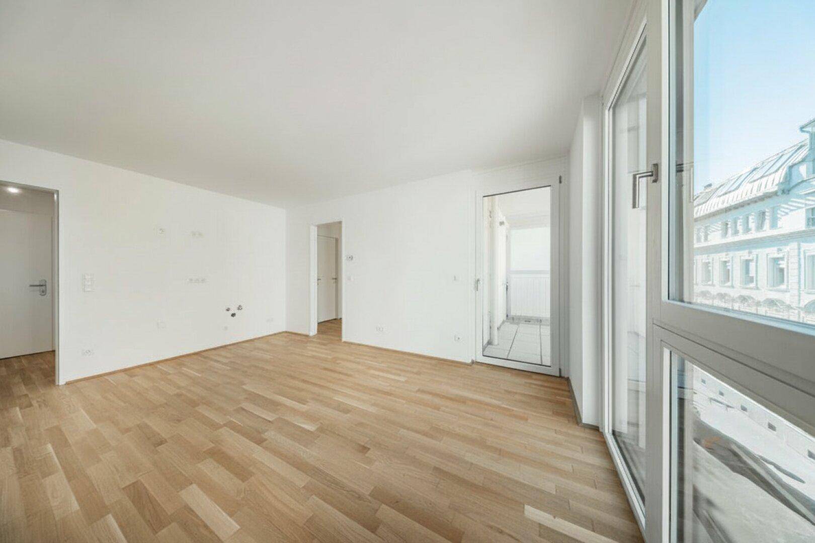 Heller Wohnbereich mit Holzboden und Zugang zu einem Balkon, der einen Blick auf die Umgebung bietet.