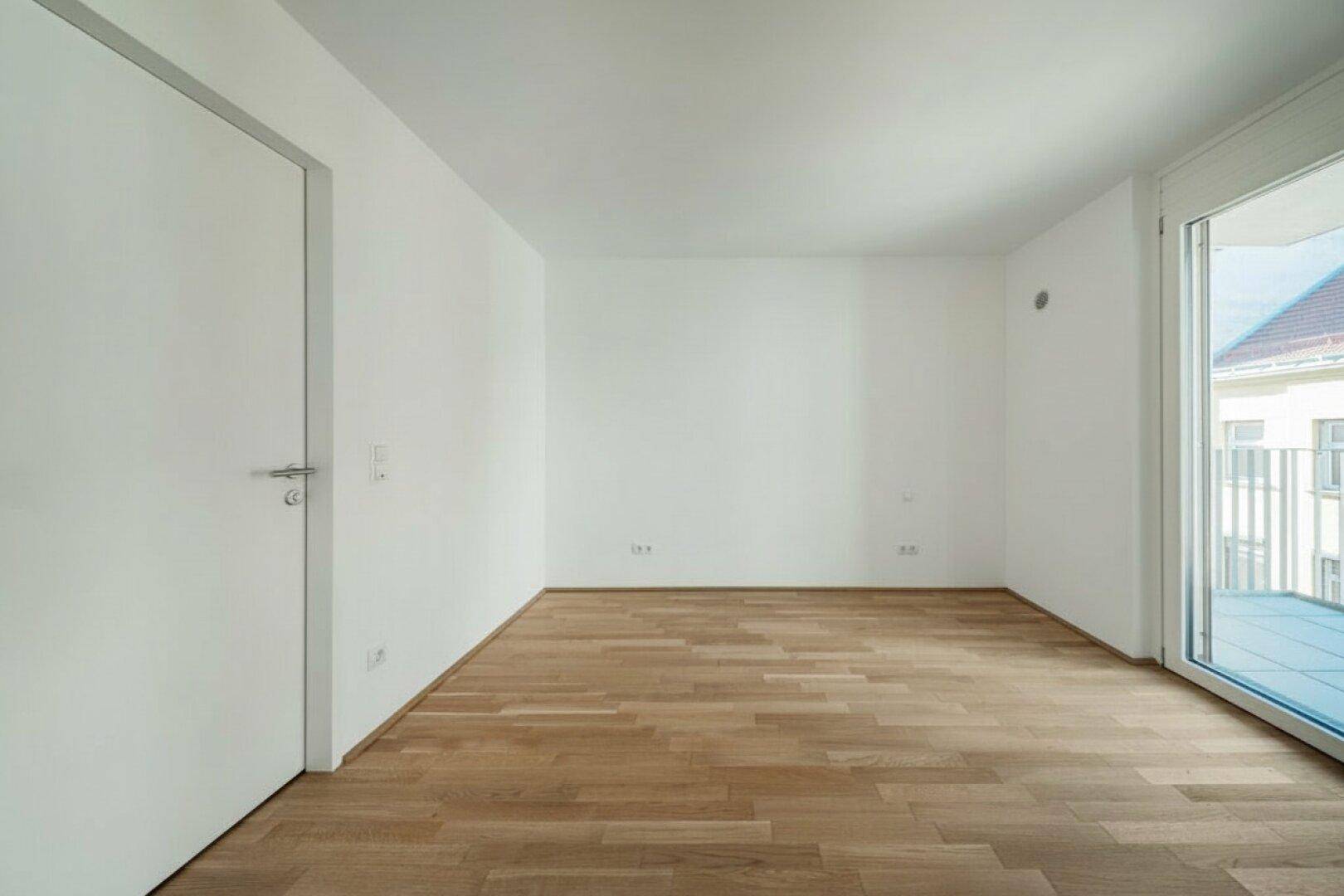 Geräumiger, heller Raum mit Parkettboden und Zugang zu einem Balkon.