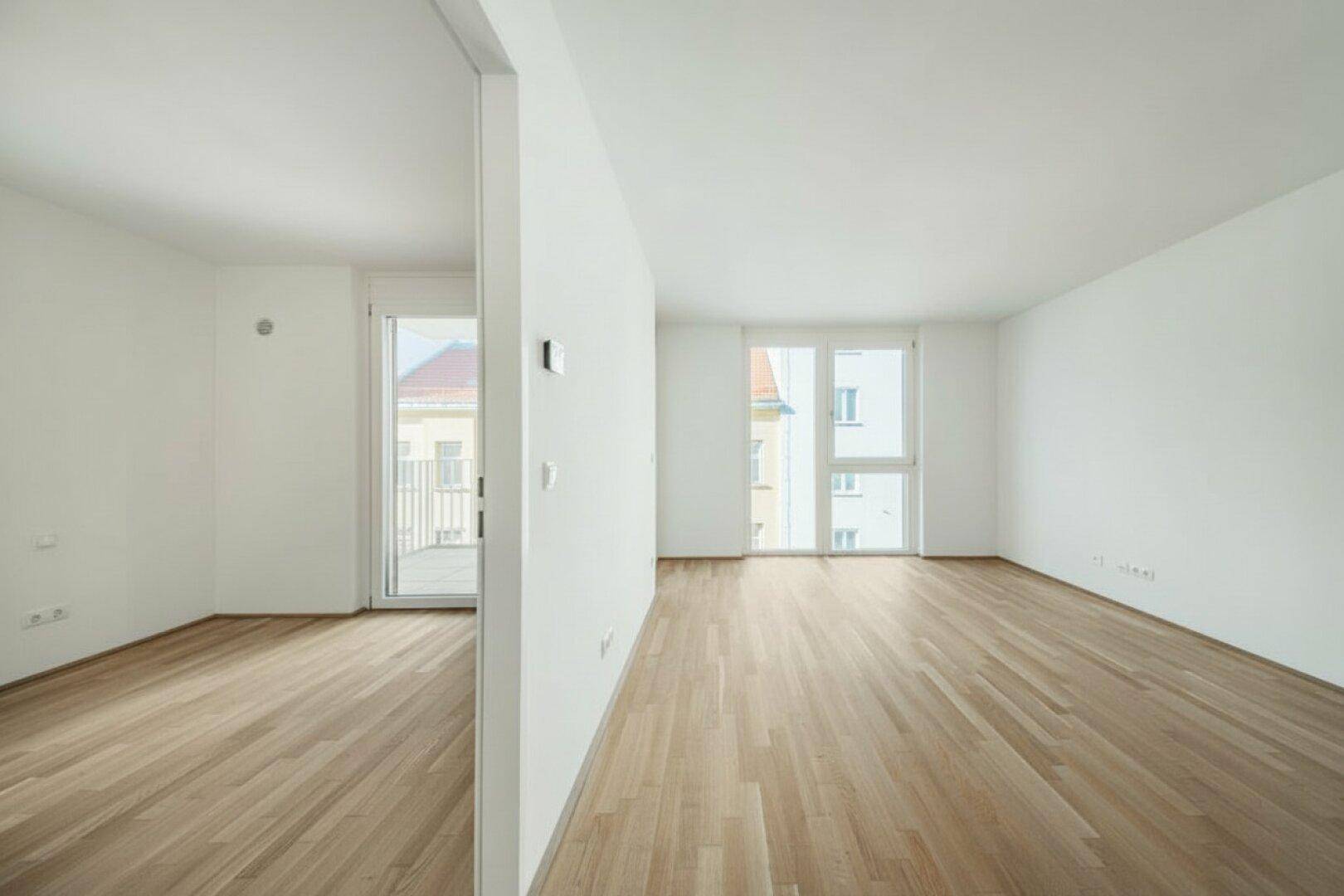 Offener, heller Raum mit Parkettboden und großen Fenstern, ideal für einen Wohnbereich.