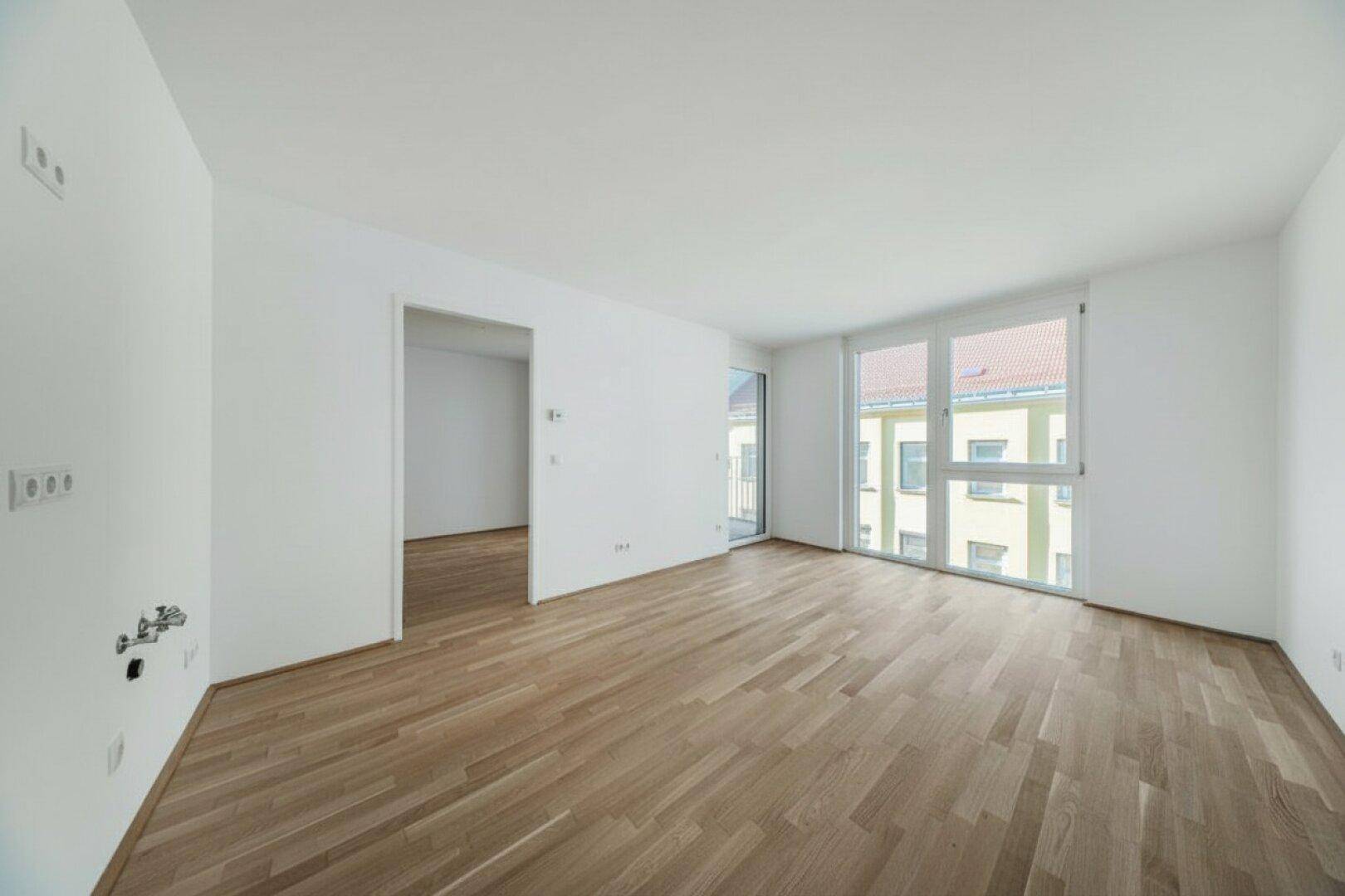 Heller Wohnbereich mit Parkettboden und Anschlüssen für eine offene Küche, mit Zugang zum Balkon.