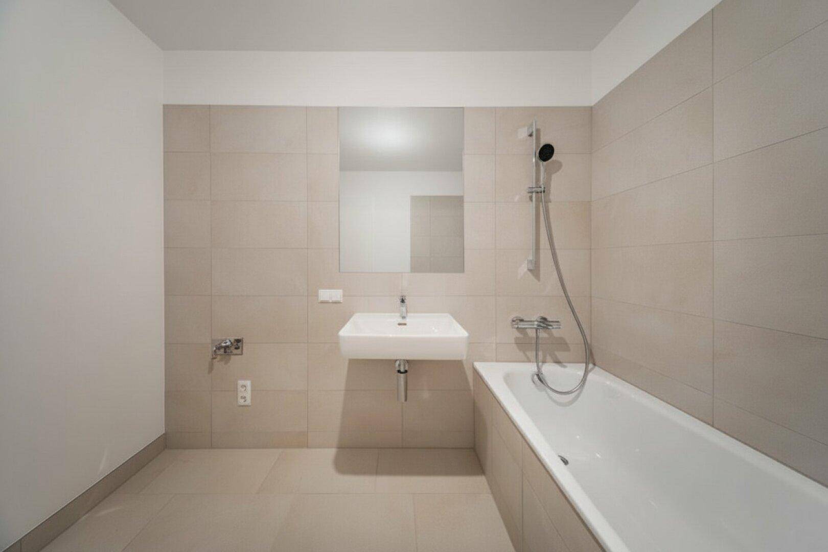 Modernes Badezimmer mit beigefarbenen Fliesen, Waschbecken und einer Badewanne mit Duschfunktion.