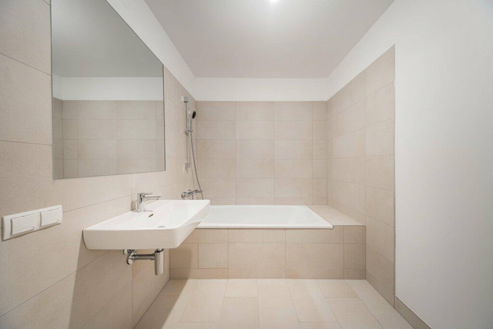 Modernes Badezimmer mit beigefarbenen Fliesen, Waschbecken und einer eingebauten Badewanne.