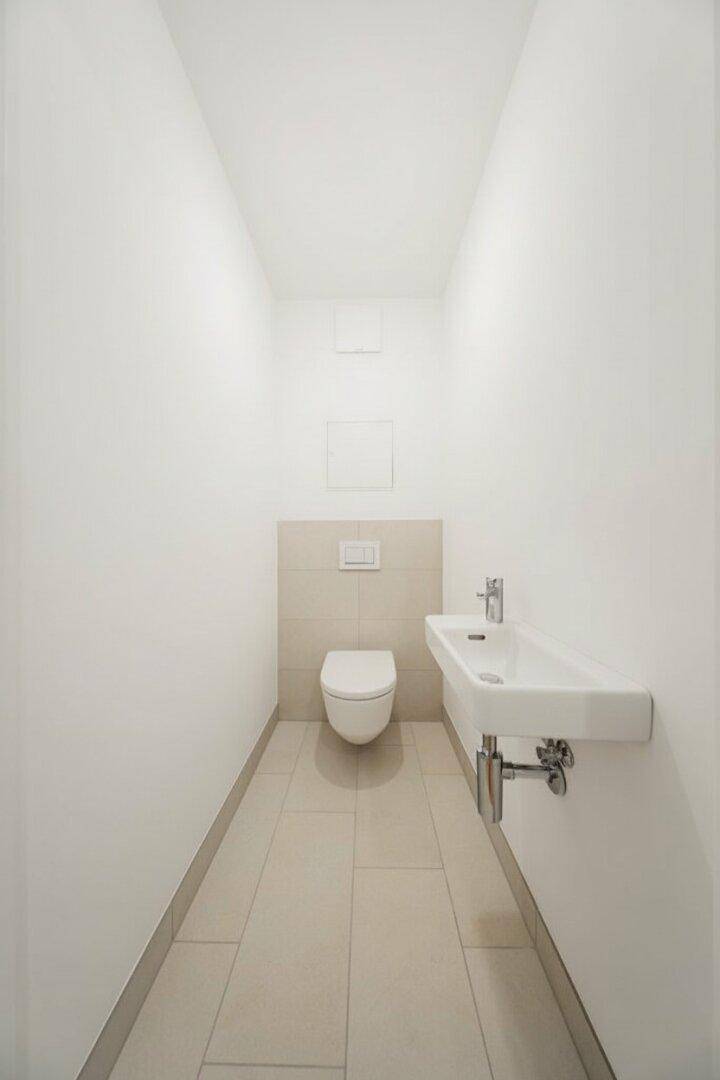 Kleines Gäste-WC mit beigefarbenen Fliesen, wandhängendem WC und Handwaschbecken.