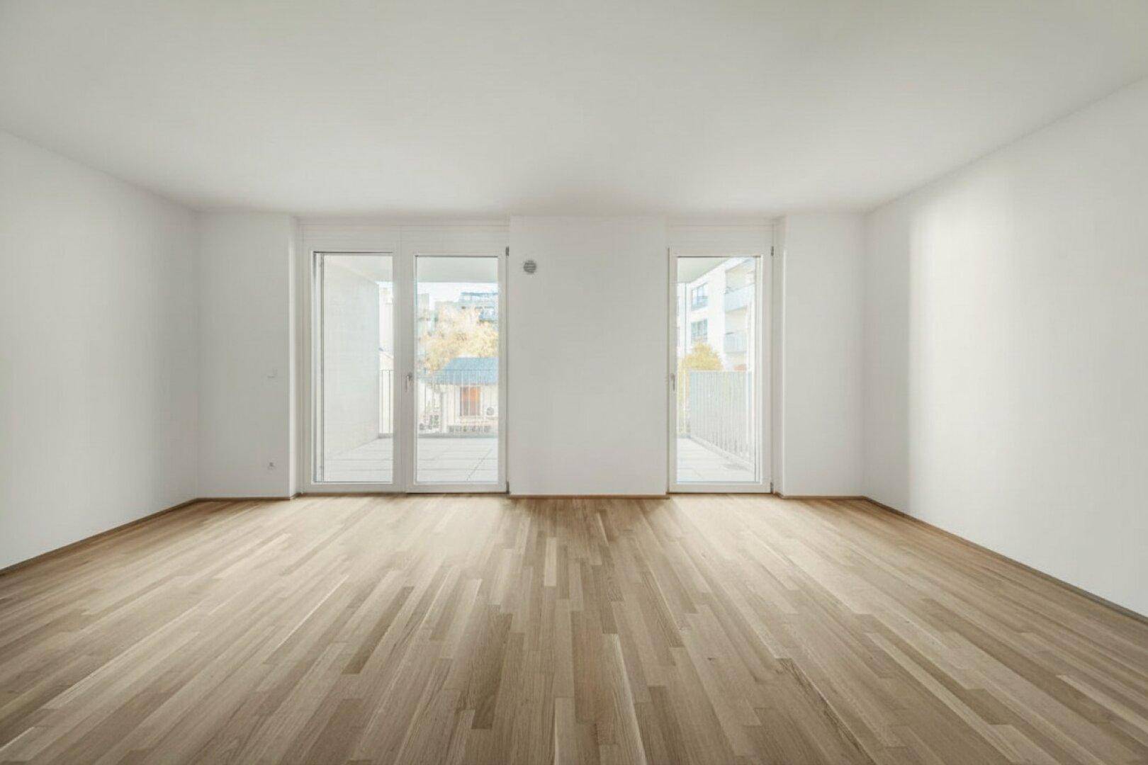 Heller, leerer Raum mit Holzboden und zwei Balkonzugängen, ideal für flexible Nutzung.