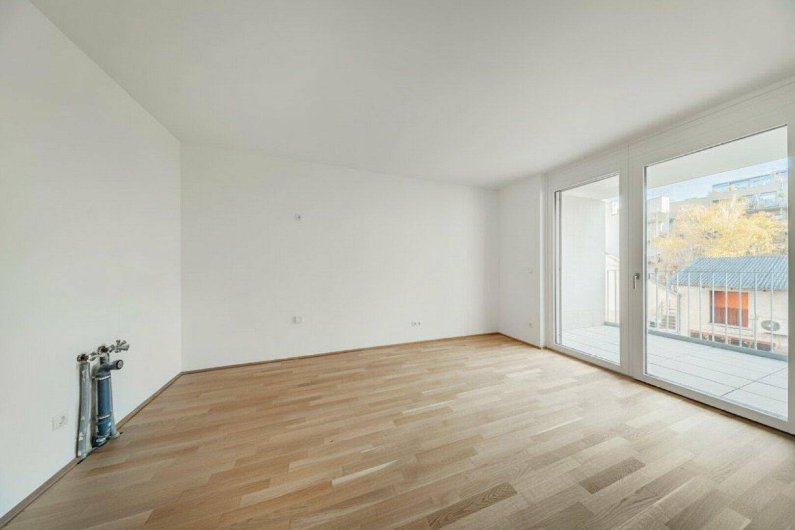 Heller Raum mit Holzboden und Balkonzugang, vorbereitet für weitere Installationen.