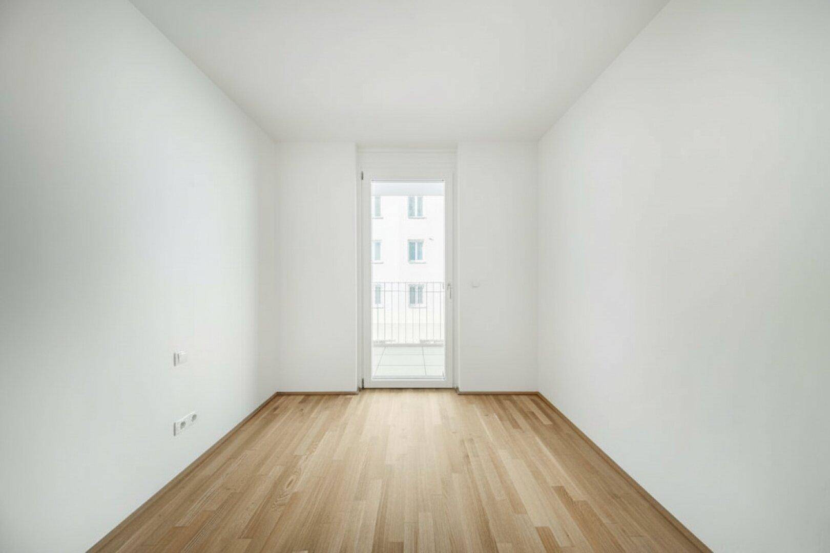 Schmaler, heller Raum mit Holzboden und Zugang zu einem kleinen Balkon.