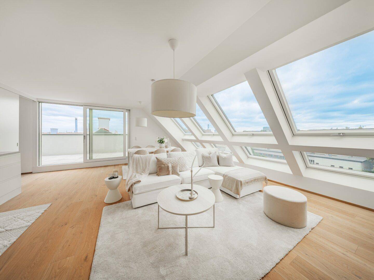 Lichtdurchflutetes Wohnzimmer im Dachgeschoss mit modernen Möbeln, Holzboden und Zugang zum Balkon.