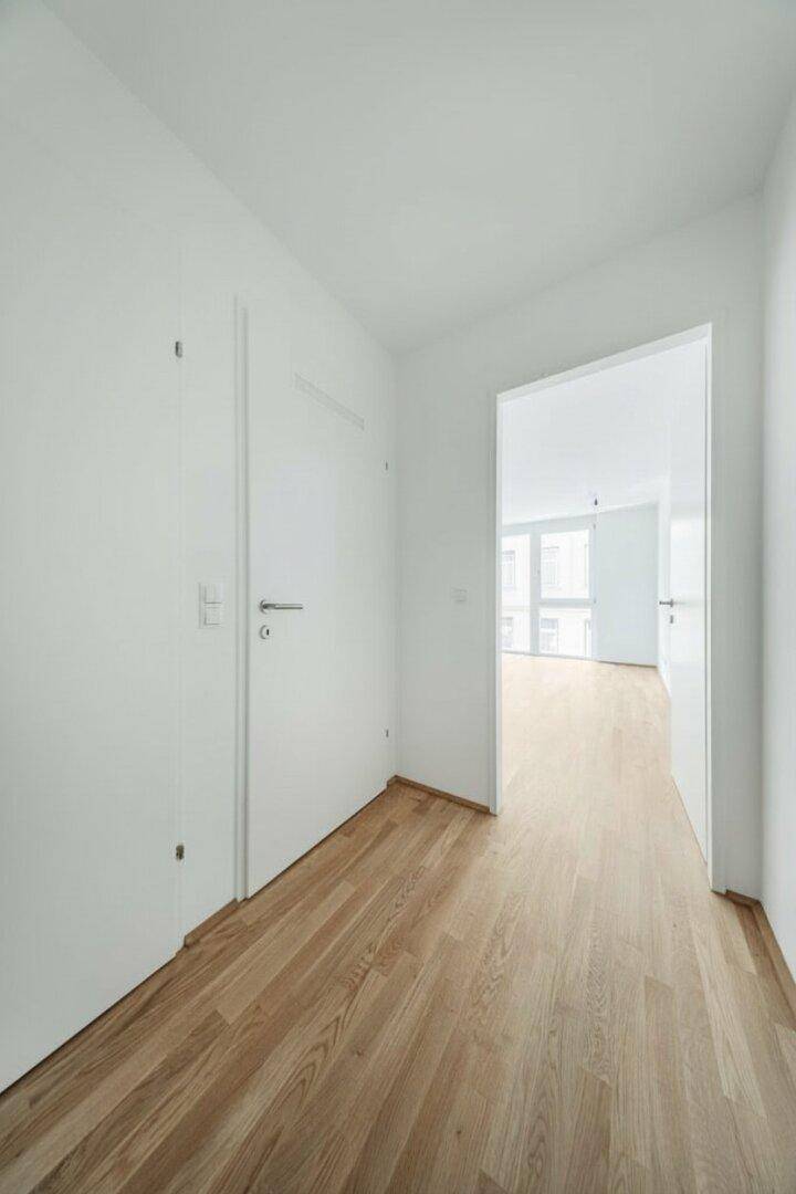 Heller Flur mit Holzboden und einer Tür, die zu einem weiteren Raum führt.