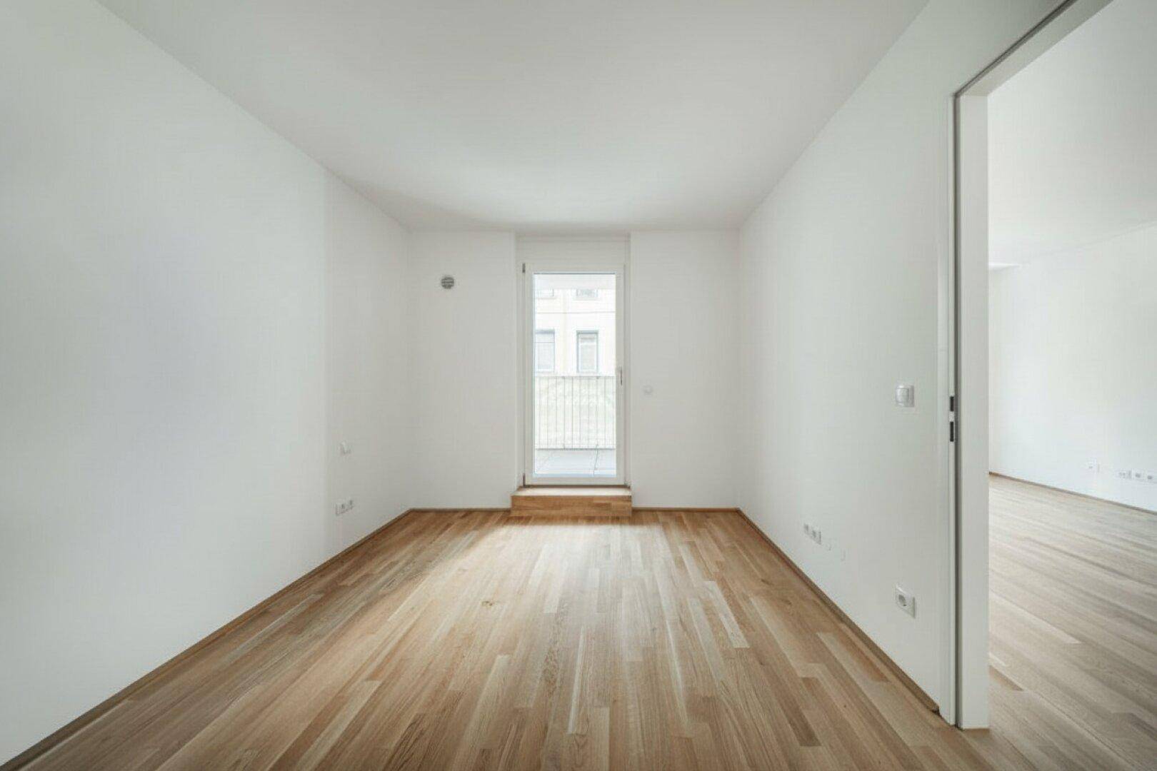 Heller, leerer Raum mit Holzboden und Zugang zu einem französischen Balkon.