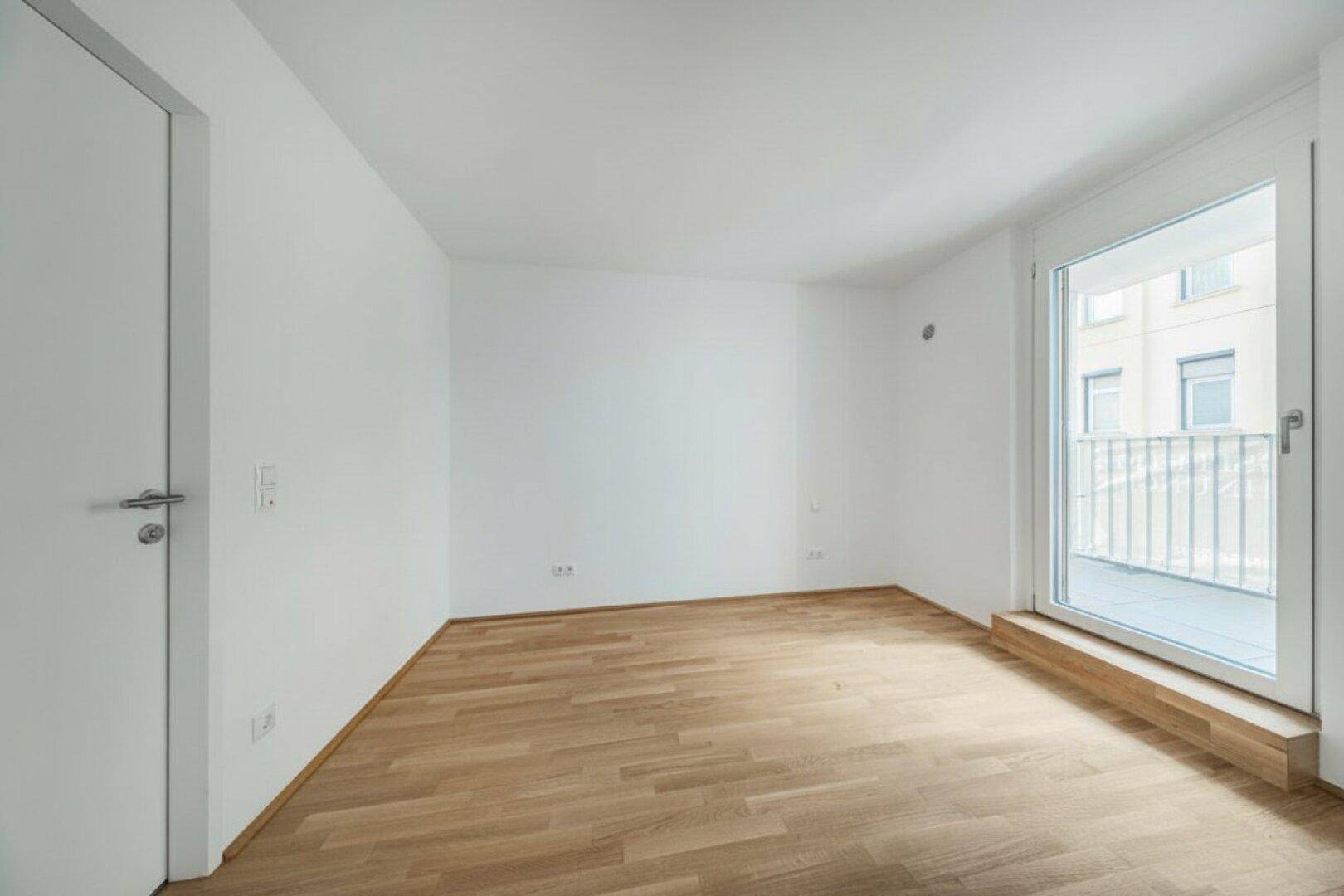 Geräumiger, leerer Raum mit Holzboden und großem Balkonzugang.