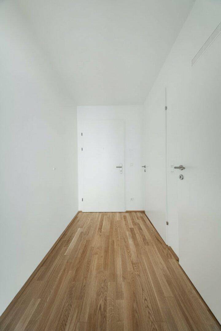 Heller Flur mit Holzboden und mehreren Türen, der verschiedene Räume verbindet.