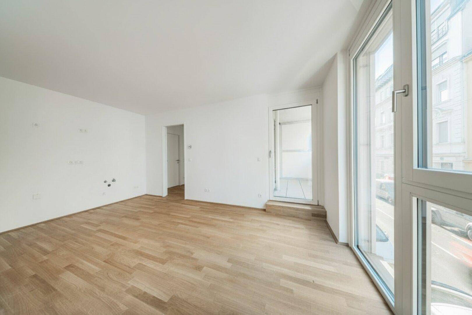 Großer, heller Raum mit Holzboden, großen Fenstern und Balkonzugang.