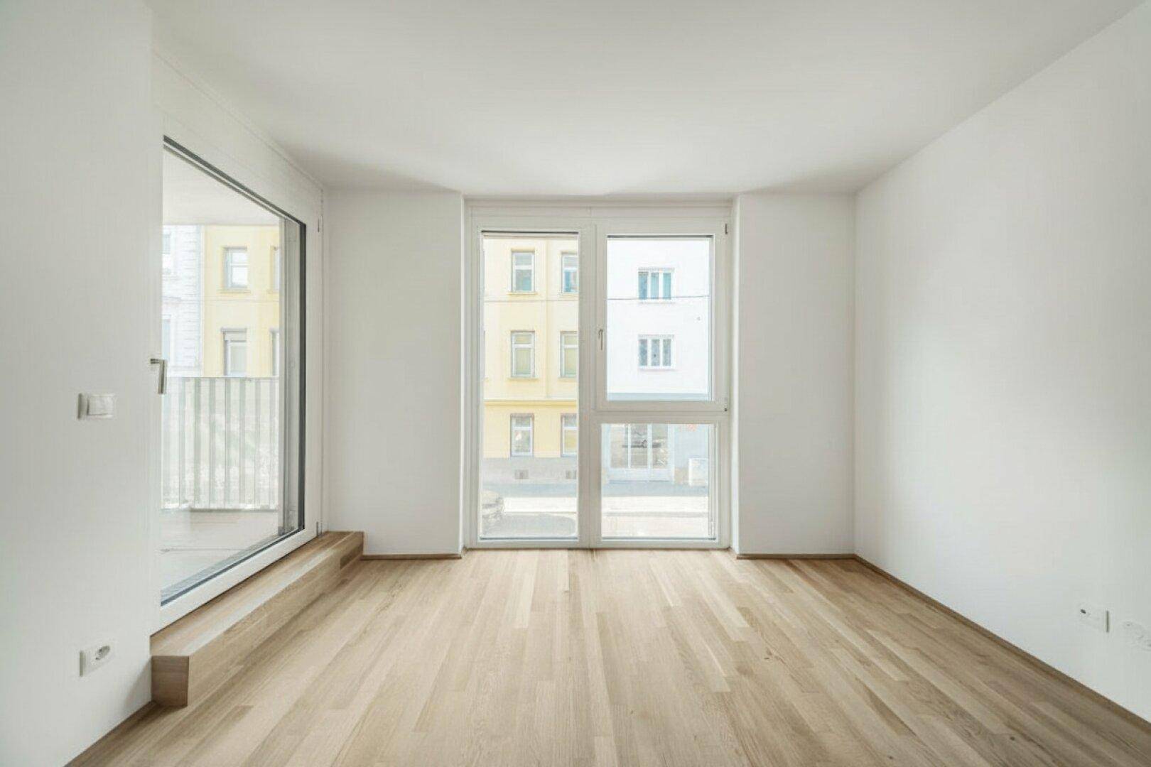 Heller Raum mit Holzboden und großen Fenstern, die viel Tageslicht hereinlassen.