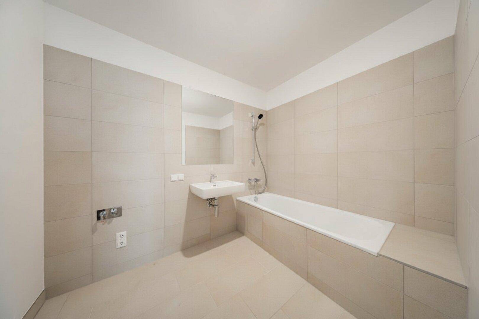 Modernes Badezimmer mit beigefarbenen Fliesen, Badewanne und Waschbecken.
