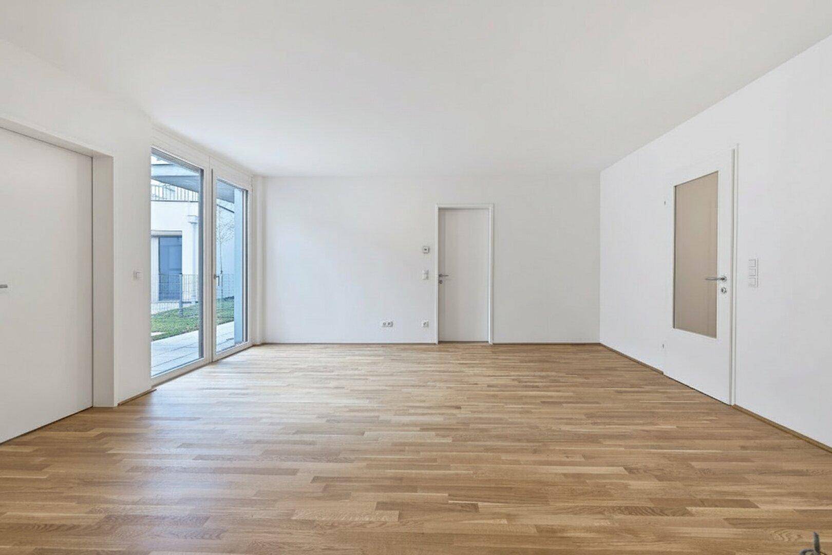 Geräumiger, heller Raum mit Holzboden und großen Fenstern zum Garten.