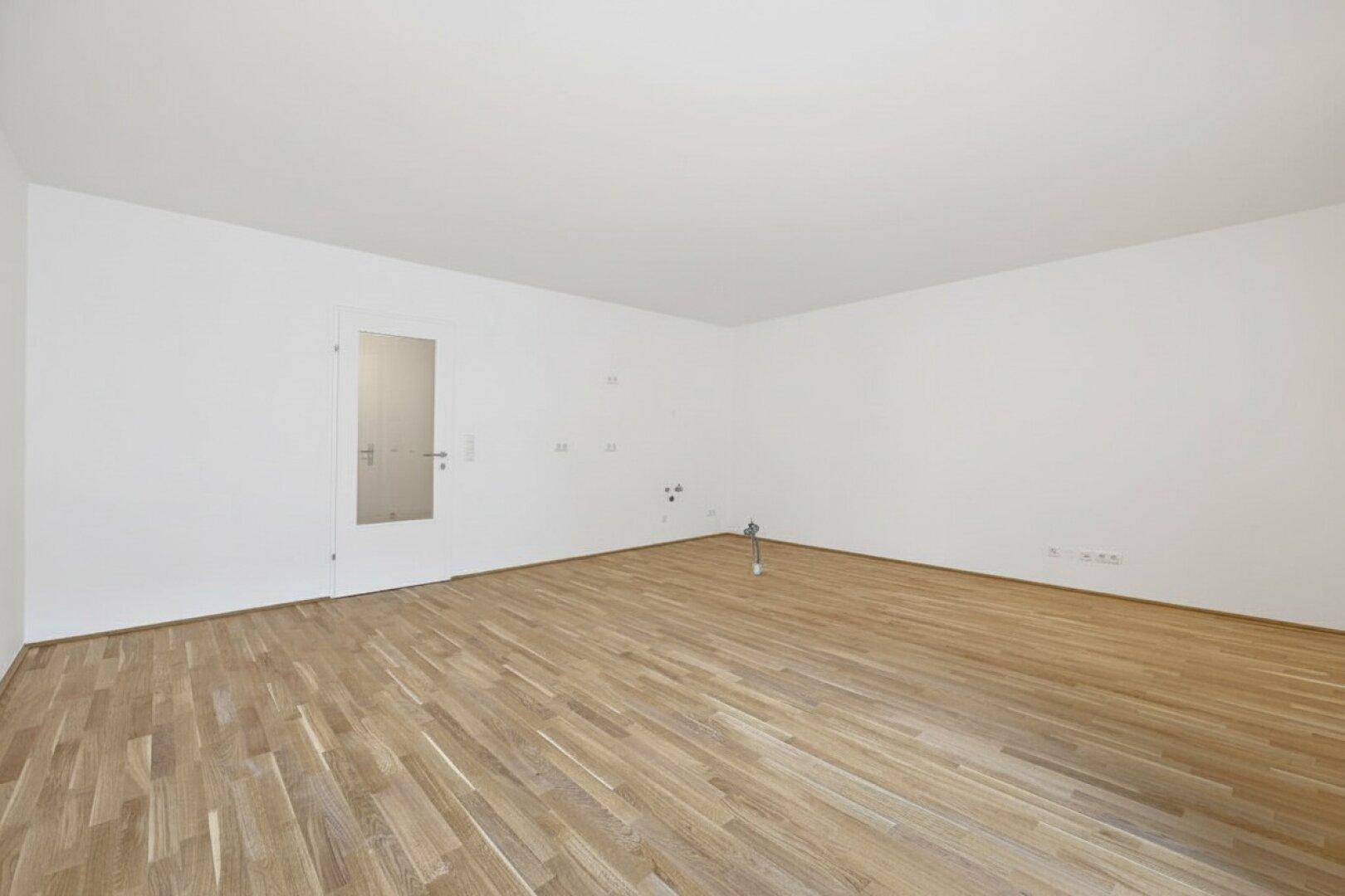 Heller Raum mit Holzboden und Anschlüssen für eine zukünftige Küche.