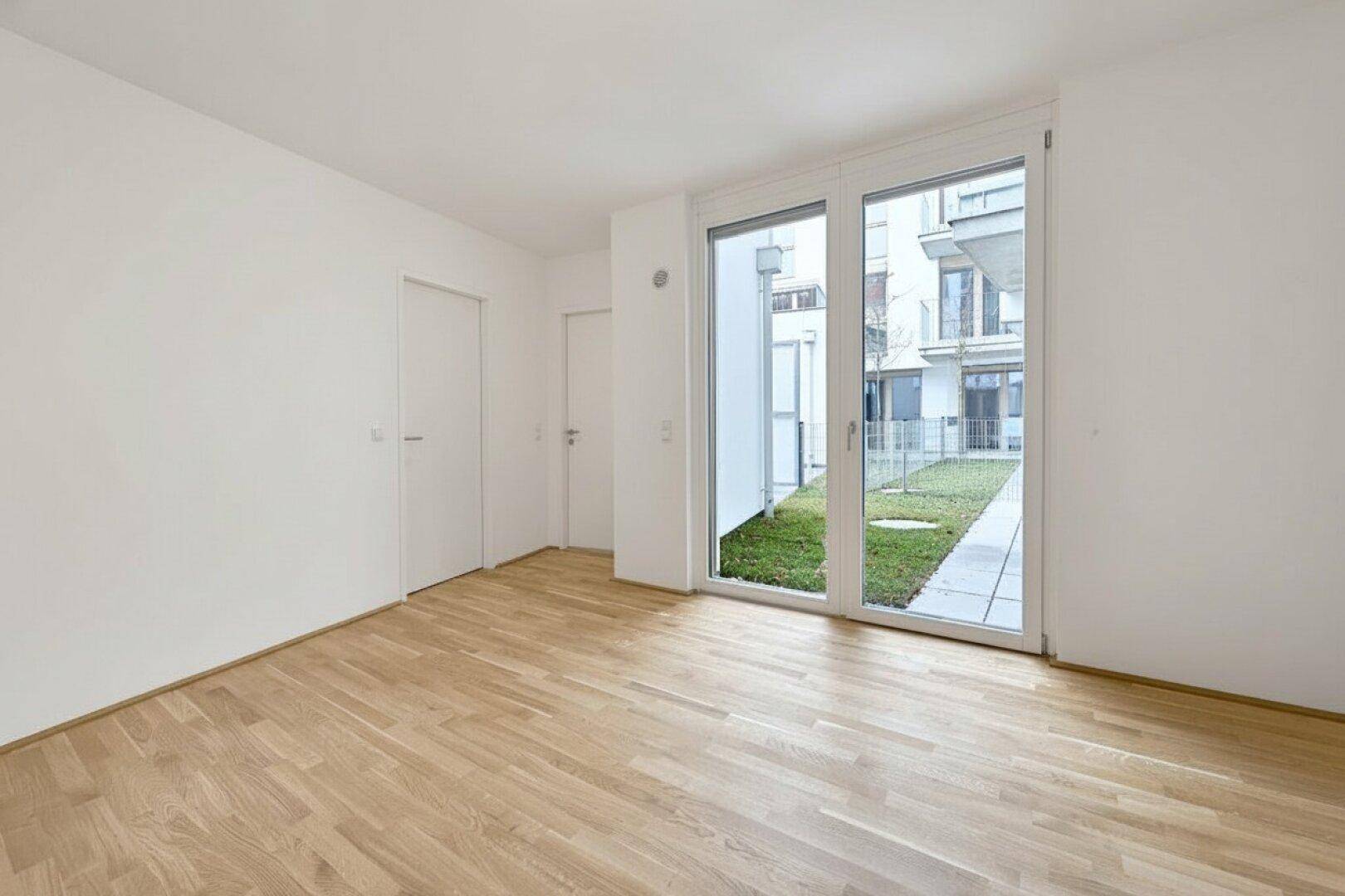 Geräumiger, heller Raum mit Holzboden und großen Fenstern mit Blick ins Grüne.