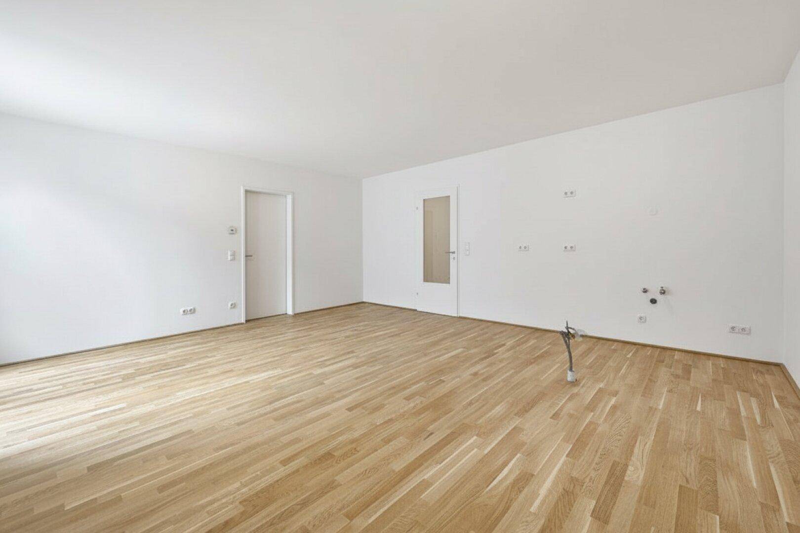 Heller Raum mit Holzboden und Anschlüssen für eine zukünftige Küche.
