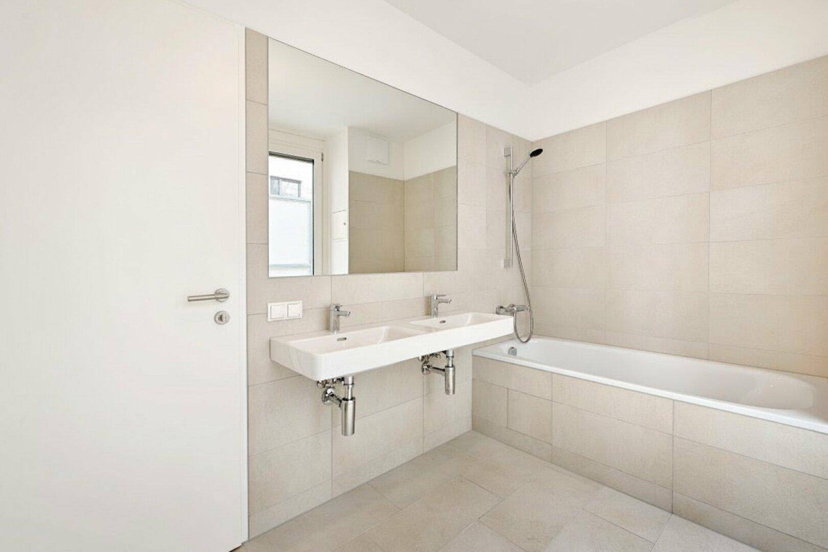 Modernes Badezimmer mit Doppelwaschbecken, Badewanne und großen Fliesen.