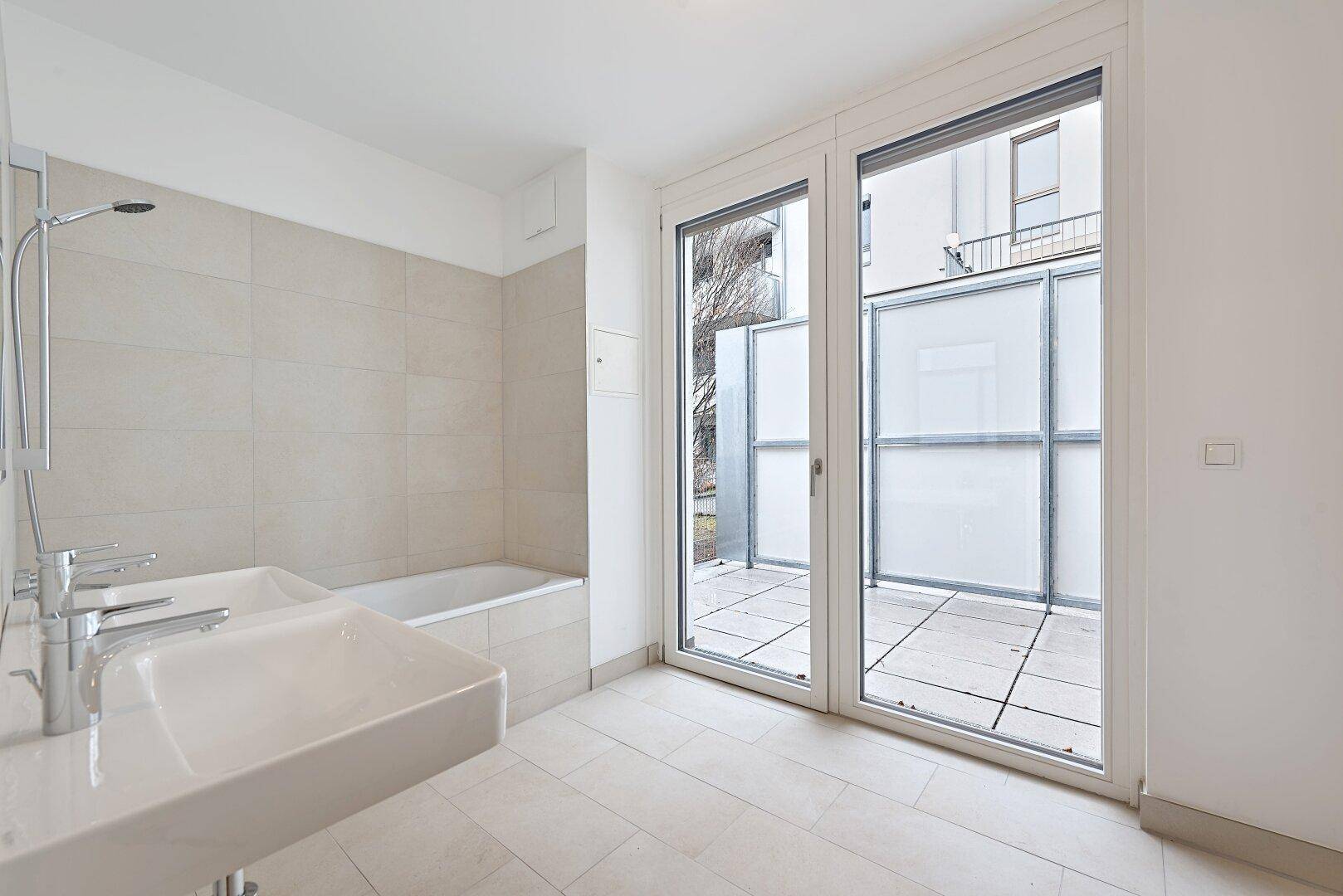 Helles Badezimmer mit Doppelwaschbecken, Badewanne und Zugang zur Terrasse.