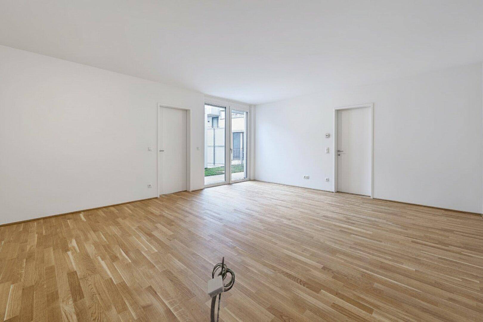 Großer, heller Raum mit Holzboden und Zugang zu einem Außenbereich.