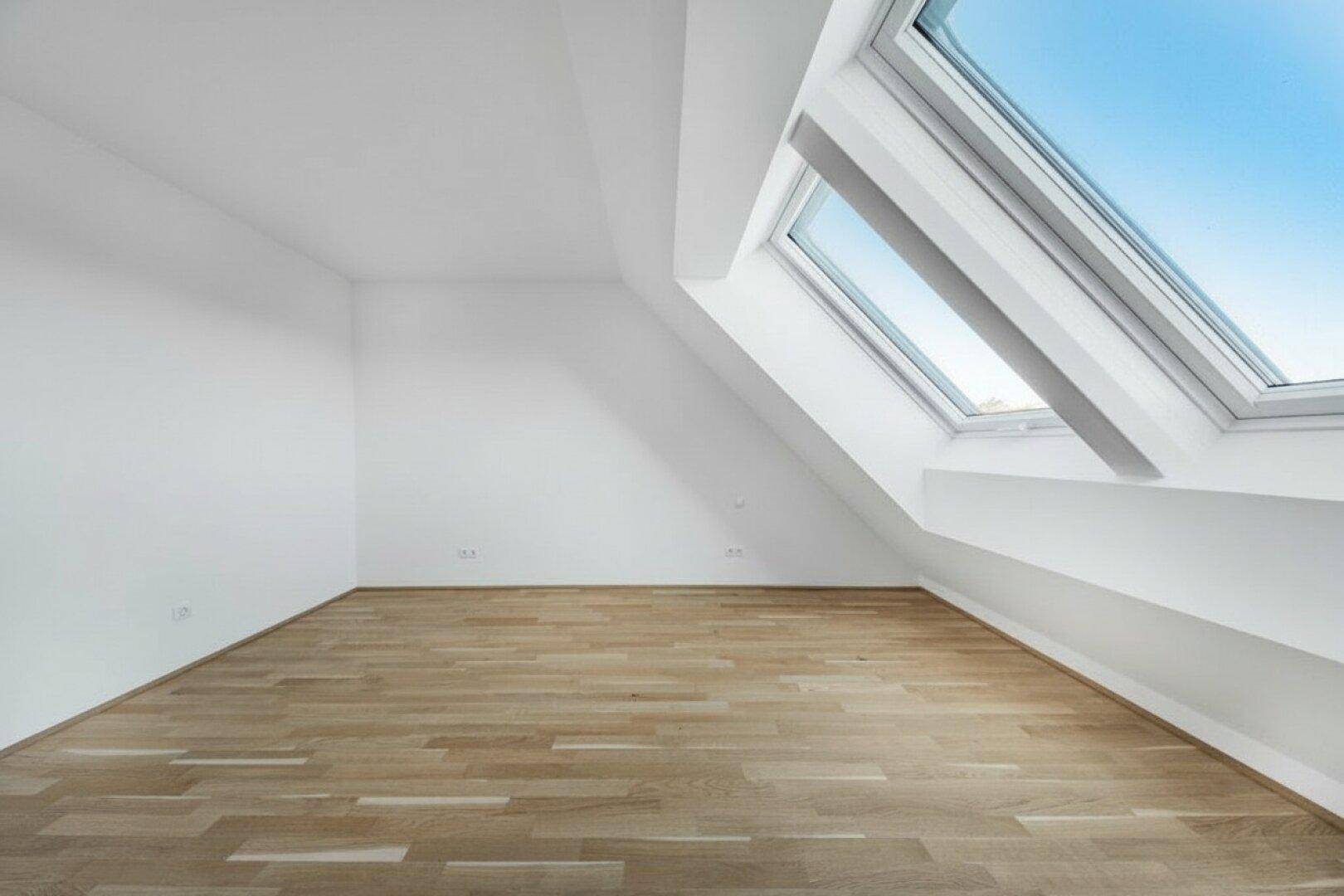 Lichtdurchfluteter Raum im Dachgeschoss mit Holzboden, weißen Wänden und großem Dachfenster.