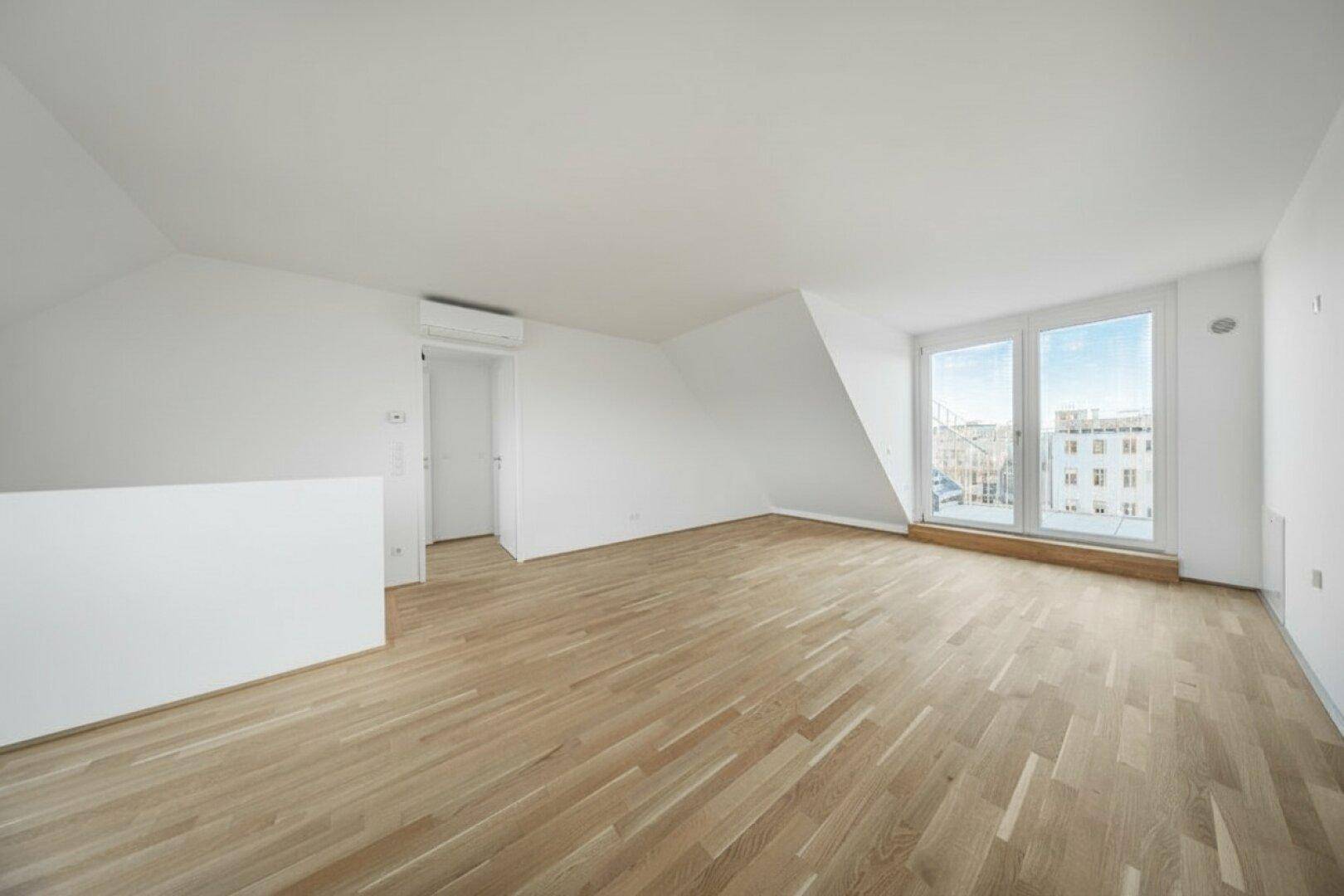 Heller Raum mit Holzboden, bodentiefen Fenstern, schräger Decke und Klimaanlage.