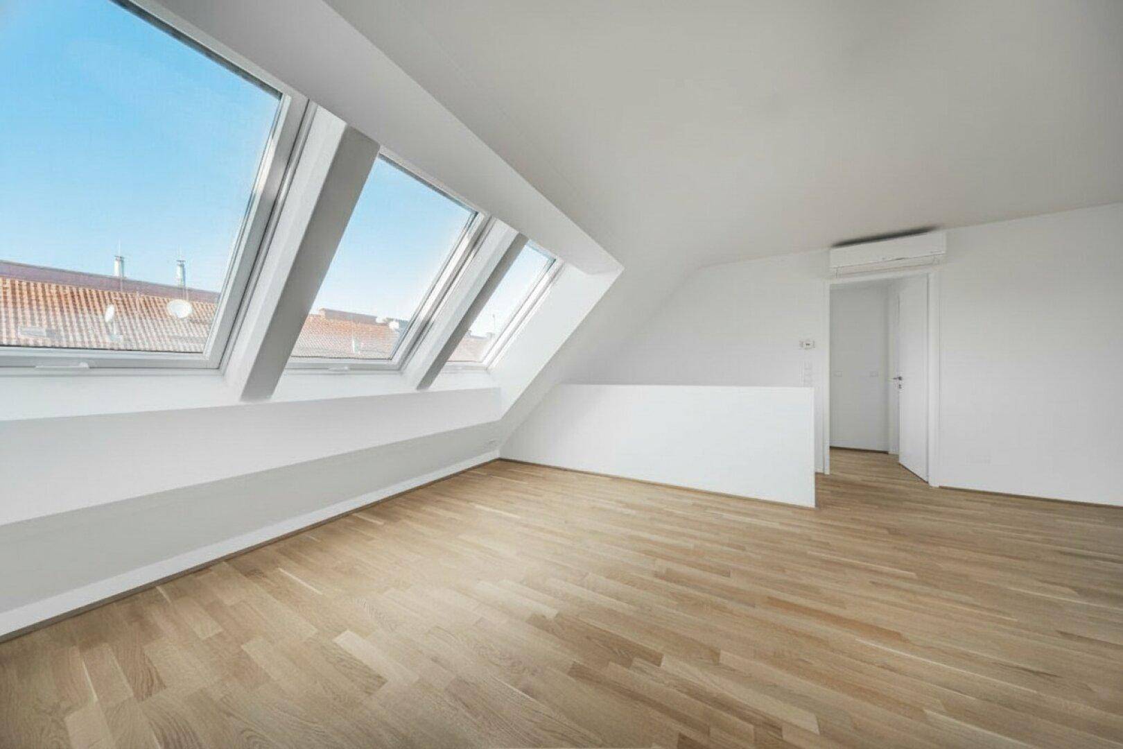 Lichtdurchfluteter Raum im Dachgeschoss mit Holzboden, weißen Wänden und mehreren Dachfenstern.