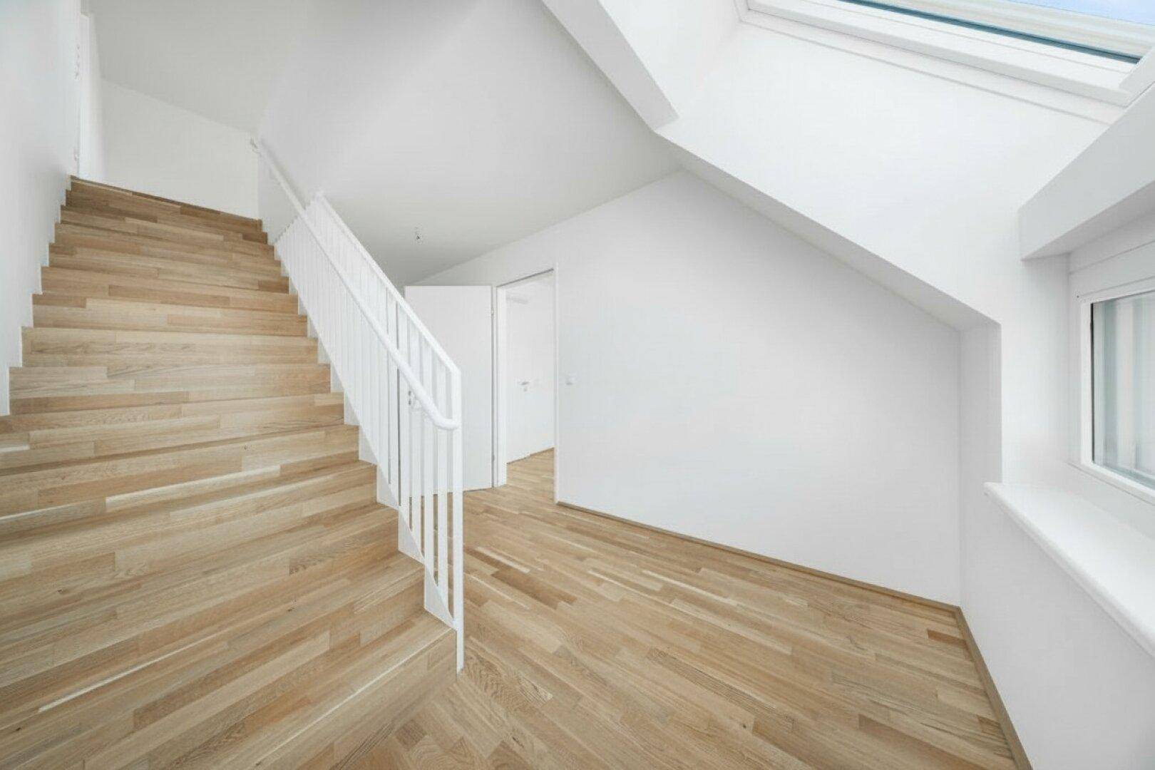 Heller Flurbereich mit Holztreppe, weißem Geländer und einem Dachfenster für natürliches Licht.