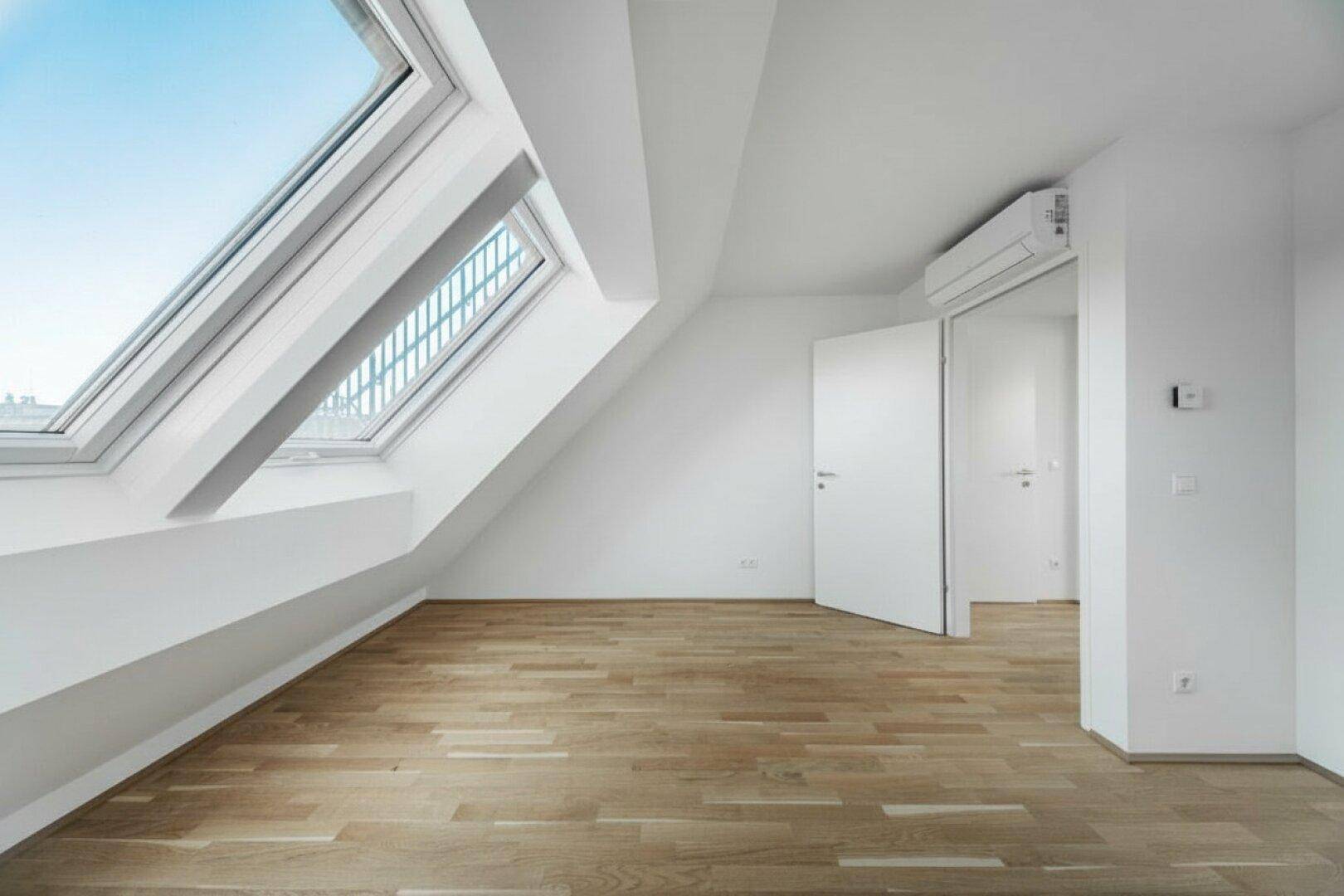 Heller Raum im Dachgeschoss mit Holzboden, Dachfenstern und installierter Klimaanlage.