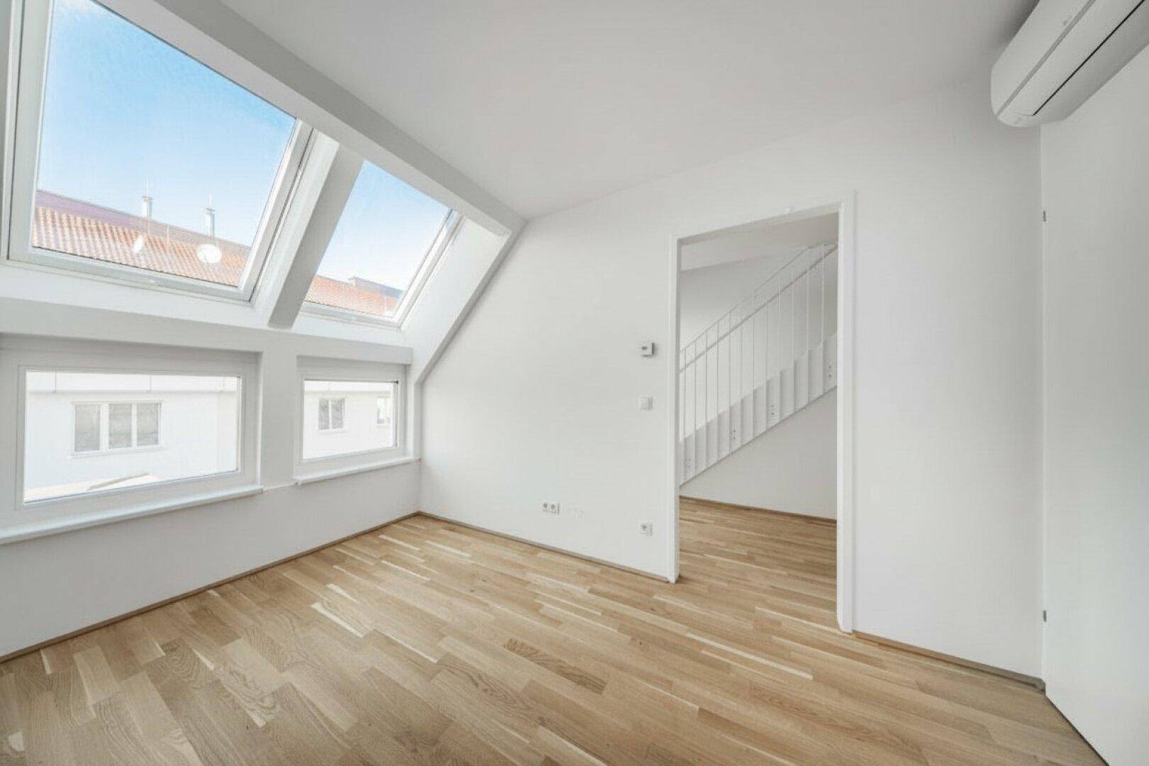 Heller Raum mit Dachfenstern, Holzboden und Zugang zu einer Treppe.