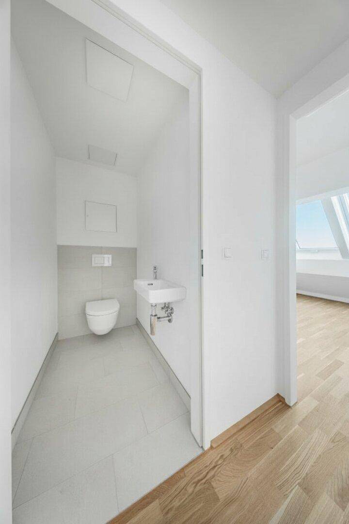 Modernes Gäste-WC mit Wand-WC, kleinem Waschbecken und hellen Fliesen.