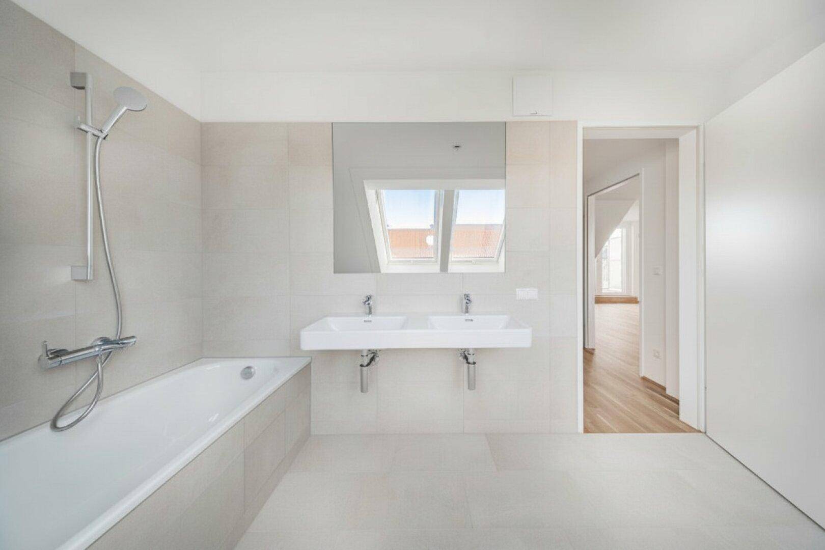 Modernes Badezimmer mit Doppelwaschbecken, Badewanne und hellen Fliesen.