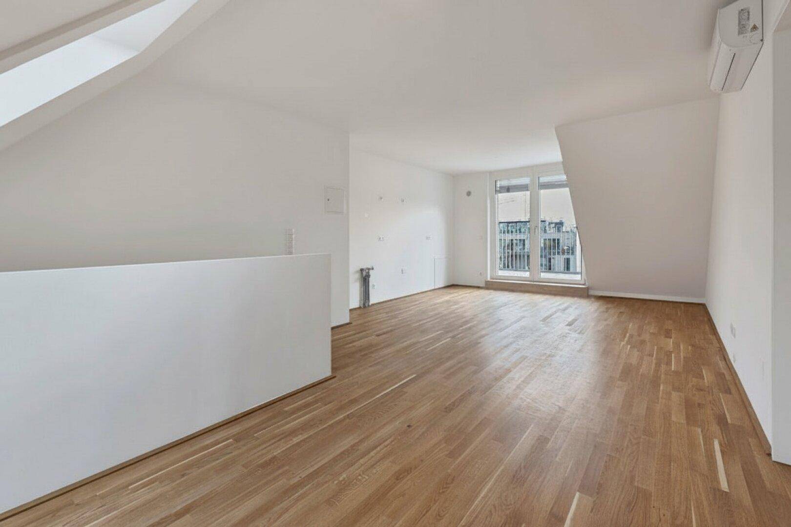 Leerer Raum mit Holzboden, Dachschrägen und Zugang zu einem Balkon.