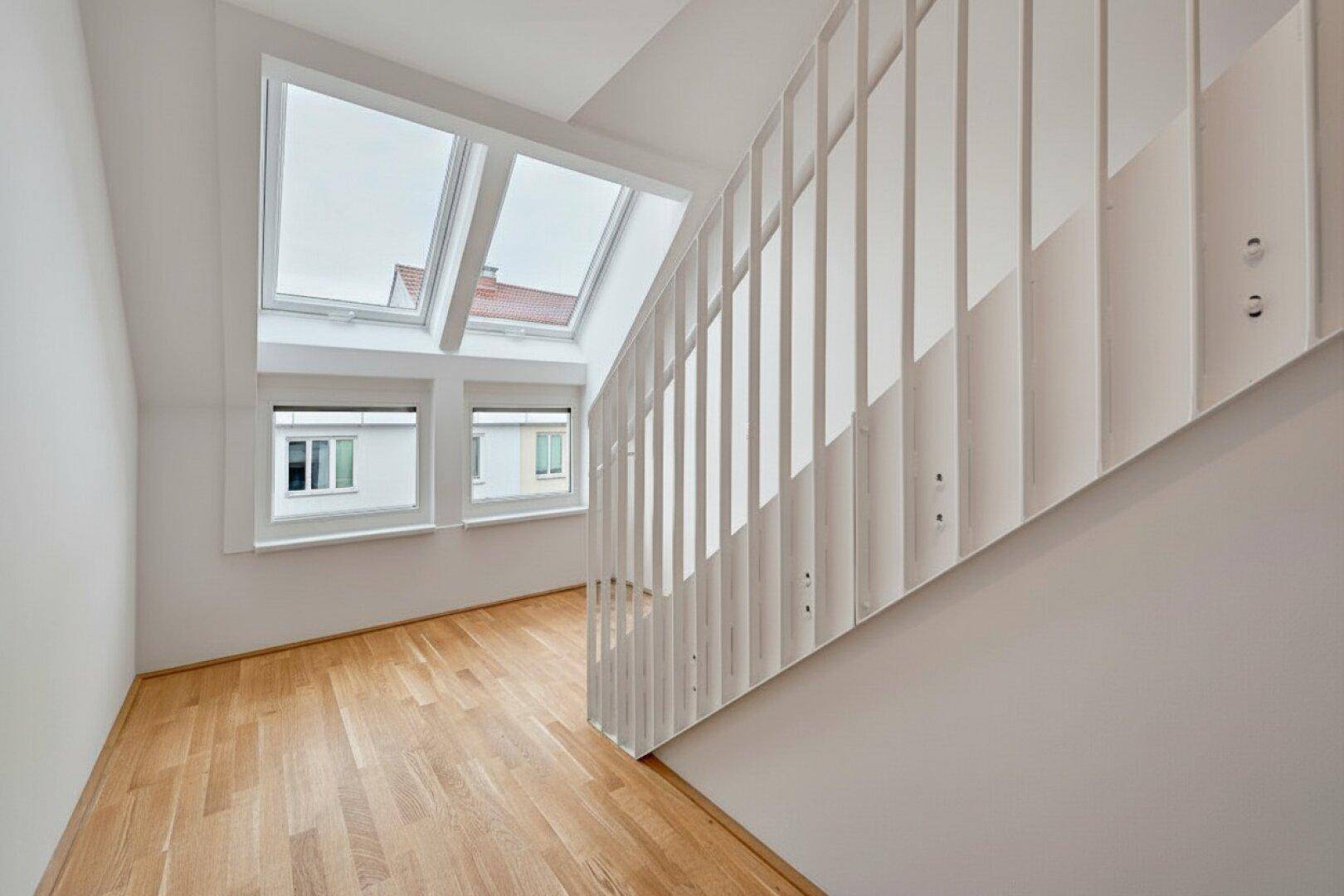 Heller Treppenbereich mit Holzboden, modernen Geländern und mehreren Dachfenstern.