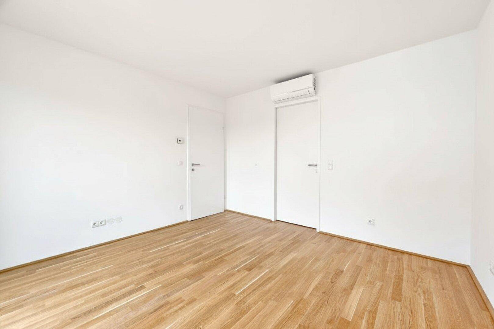 Leerer Raum mit Holzboden, weißen Wänden und Klimaanlage, bereit zur individuellen Gestaltung.