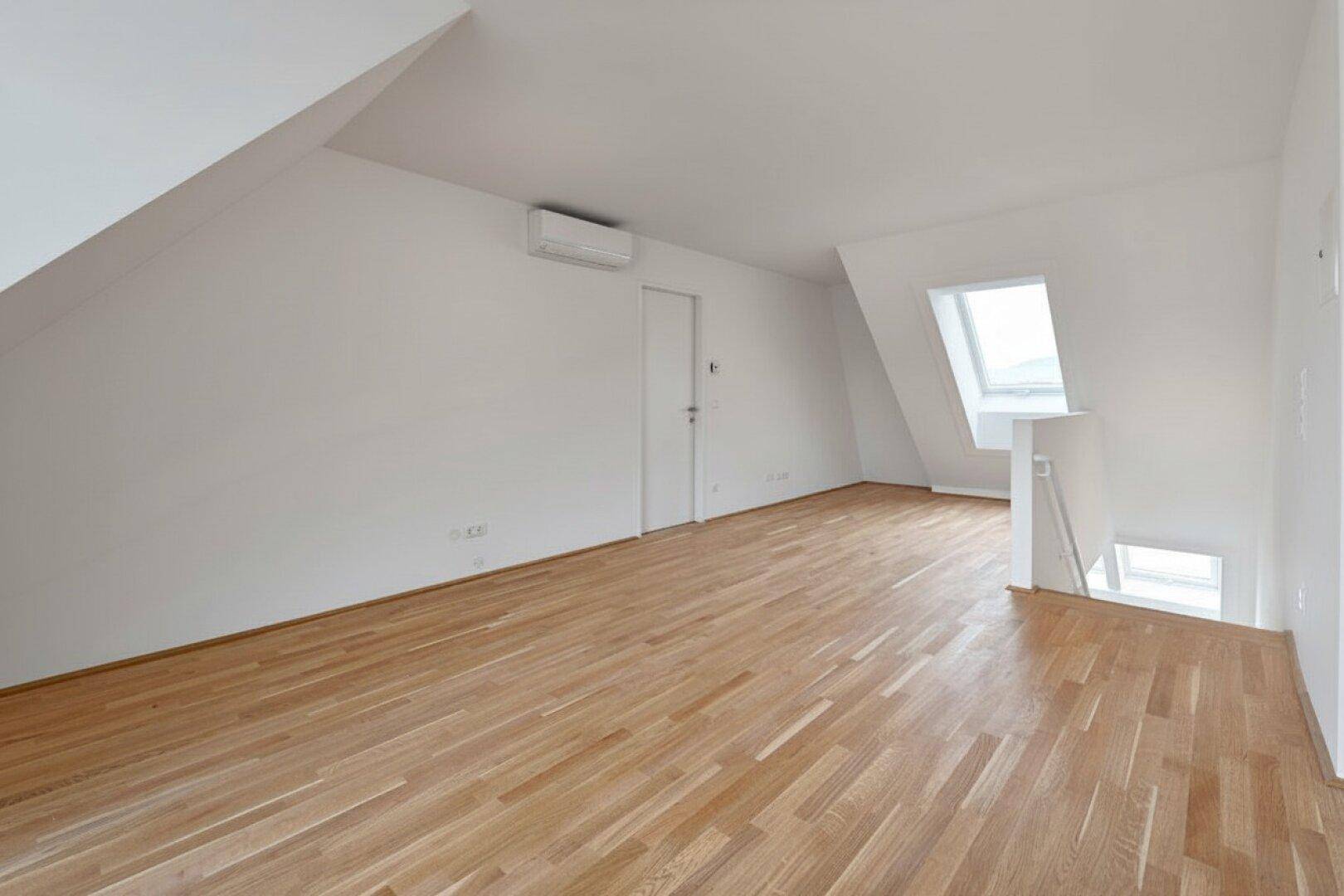 Geräumiger, leerer Raum mit Holzboden, Dachschrägen und einem Dachfenster für viel Licht.