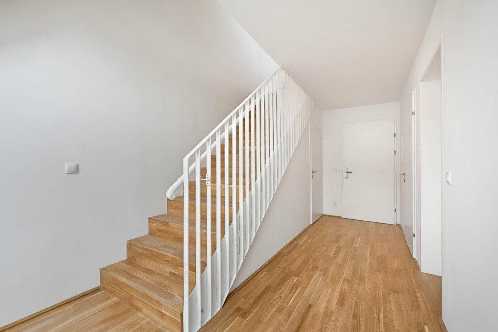 Heller Eingangsbereich mit Holztreppe und modernem Geländer, der die Etagen verbindet.