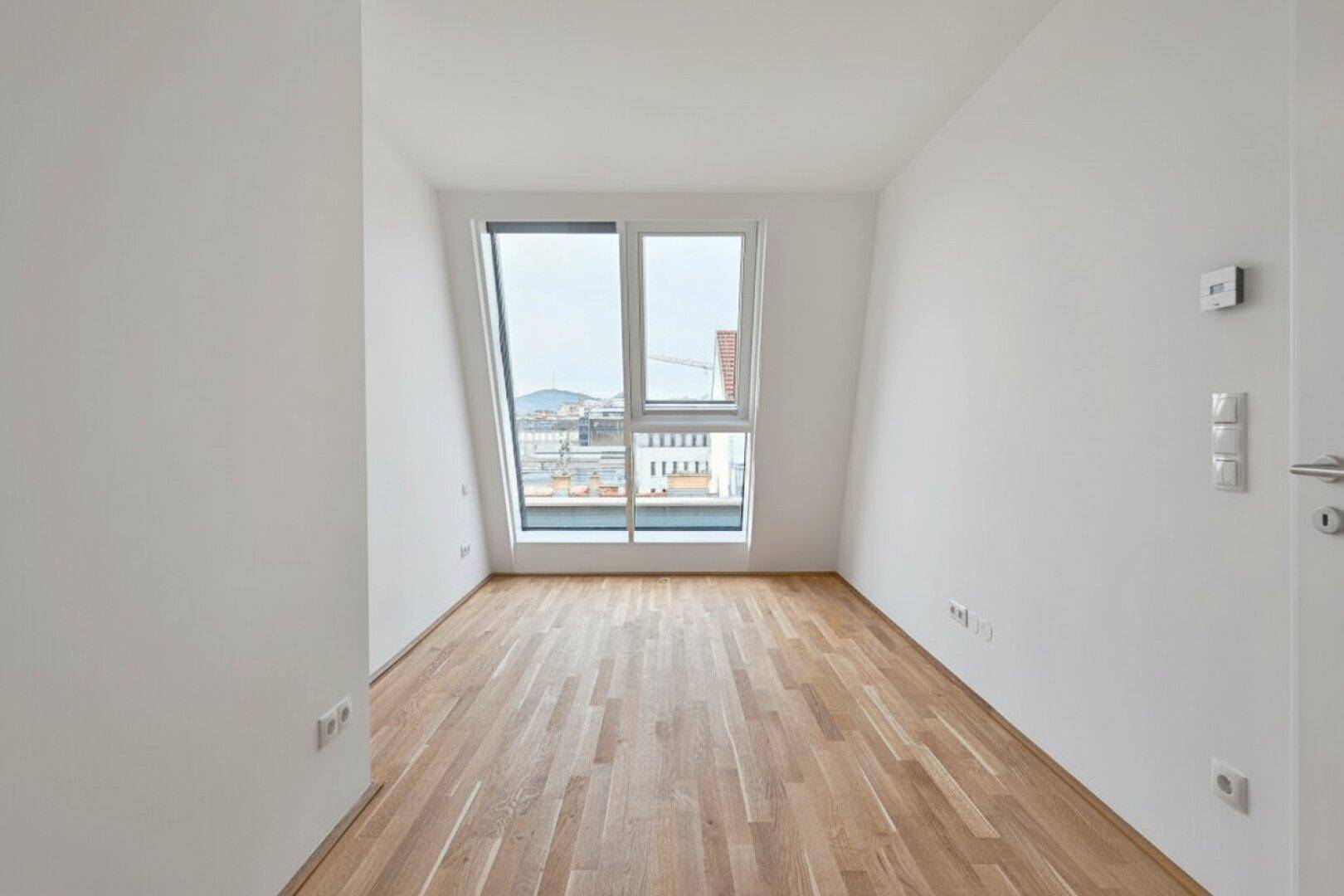 Leerer Raum mit Holzboden und großem, schrägem Fenster, das eine weite Aussicht bietet.
