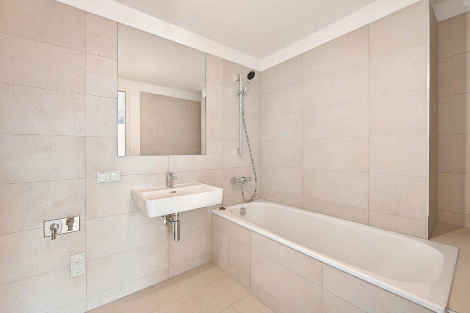 Modernes Badezimmer mit hellen Fliesen, Badewanne und integrierter Dusche sowie einem Waschbecken.