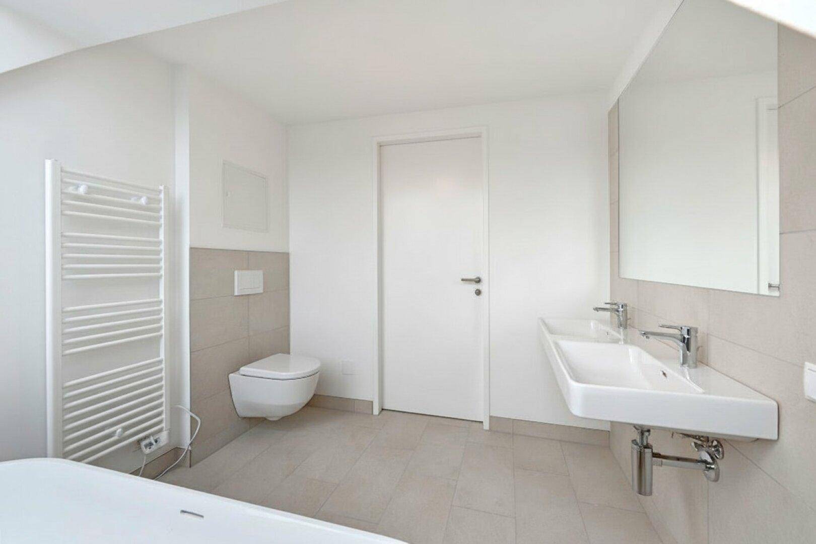 Helles Badezimmer mit Doppelwaschbecken, wandhängendem WC und beheiztem Handtuchhalter.